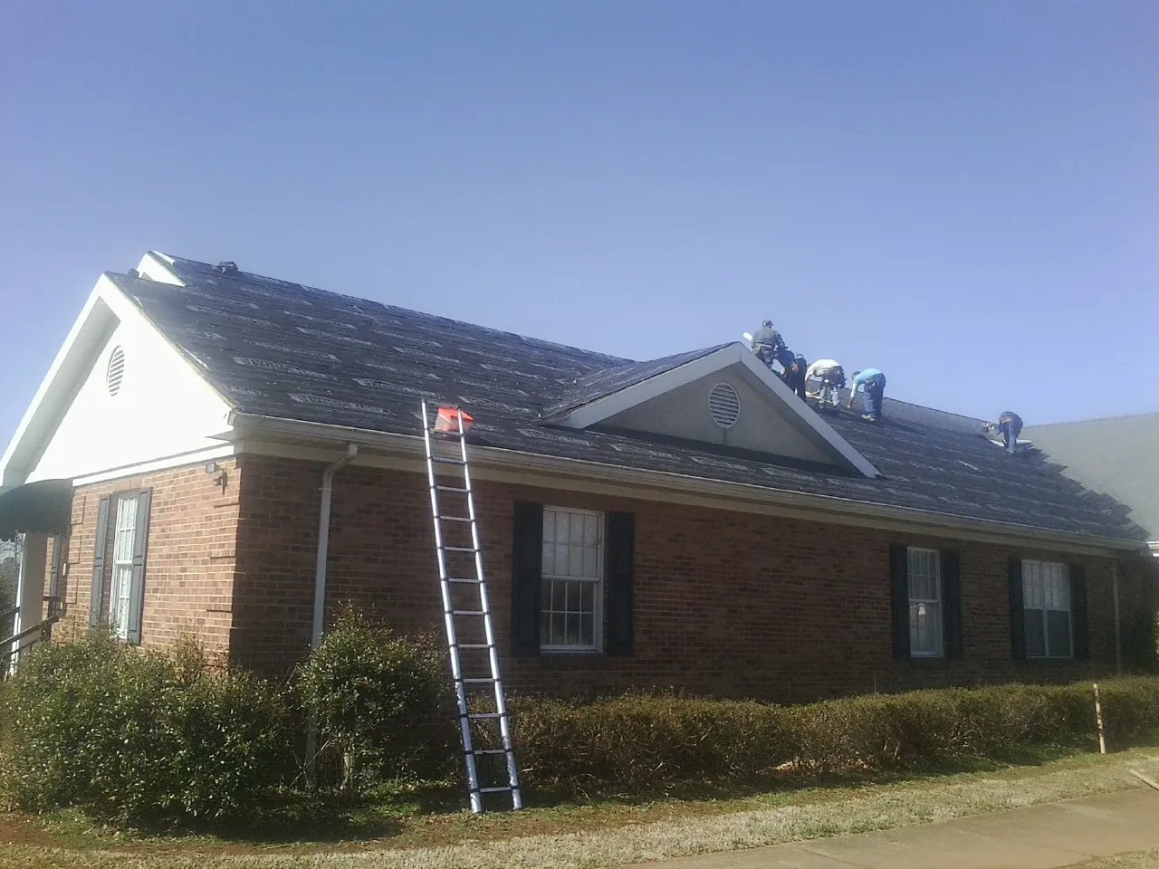 Crew tearing shingles off a brick ranch roof with a ladder set — Emergency Roof Repair work by our crew in Cordesville