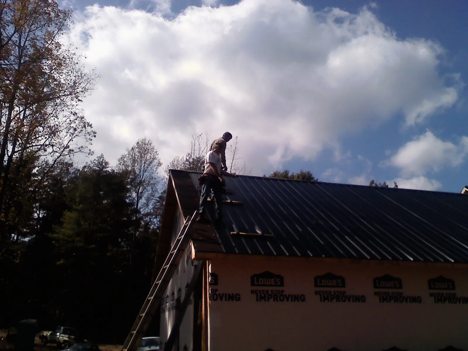 Roofer fastening dark metal panels high against a cloudy sky, from a Roof Inspection job in Cordesville